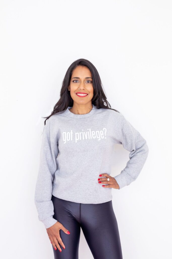 Ritu Bhasin standing with one hand on her hip and confidently smiling at the camera. She wears a grey sweatshirt with the quote "Got Privilege?" printed on it.