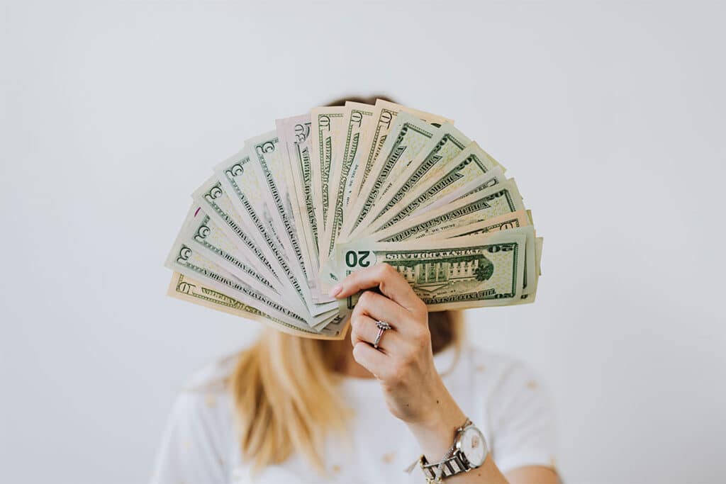 A woman with blonde hair holding up a number of $5, $50 and $20 American bills covering her face