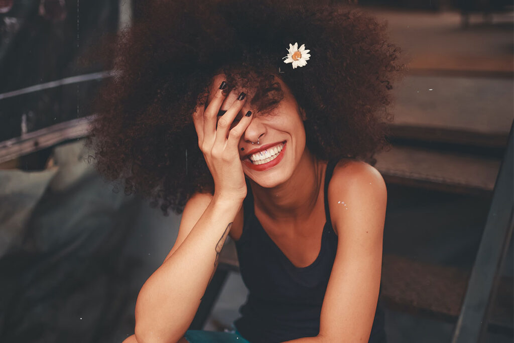 A young Black woman smiling with her head in her left hand.
