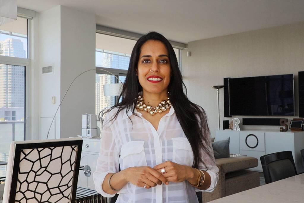 Ritu Bhasin wearing a white shirt and a gold necklace smiling.