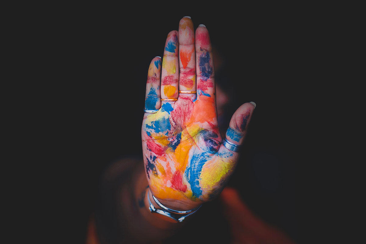 A hand held up showing the palm and fingers covered in red, yellow, orange and blue paint.