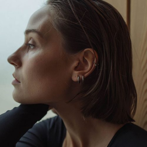 The right side profile of a white woman with short brown hair. She has one arm by the side of her face as she looks off to the left side.