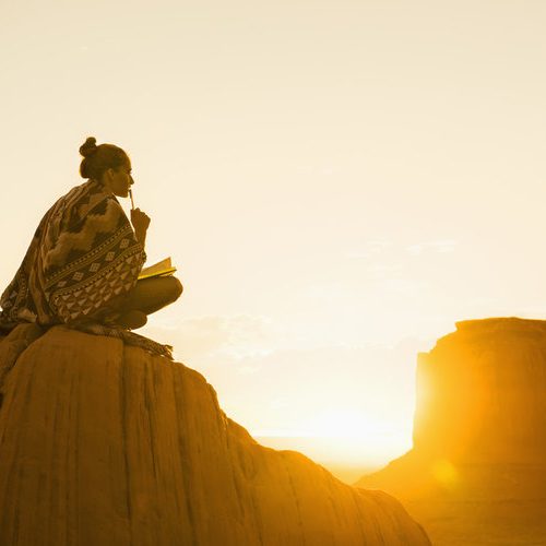 Hispanic woman sitting on rock formation in remote desert