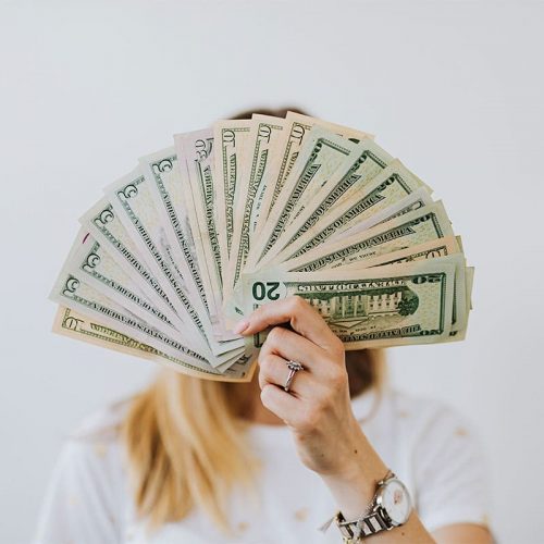 A woman with blonde hair holding up a number of $5, $50 and $20 American bills covering her face