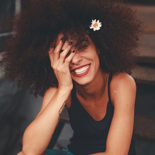 A young Black woman smiling with her head in her left hand.