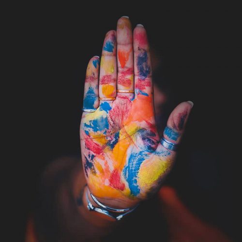 A hand held up showing the palm and fingers covered in red, yellow, orange and blue paint.