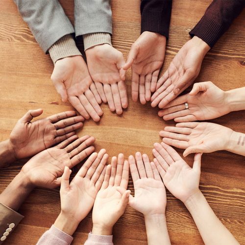 Six pairs of hands of various skin tones facing with their palms up on a wooden surface